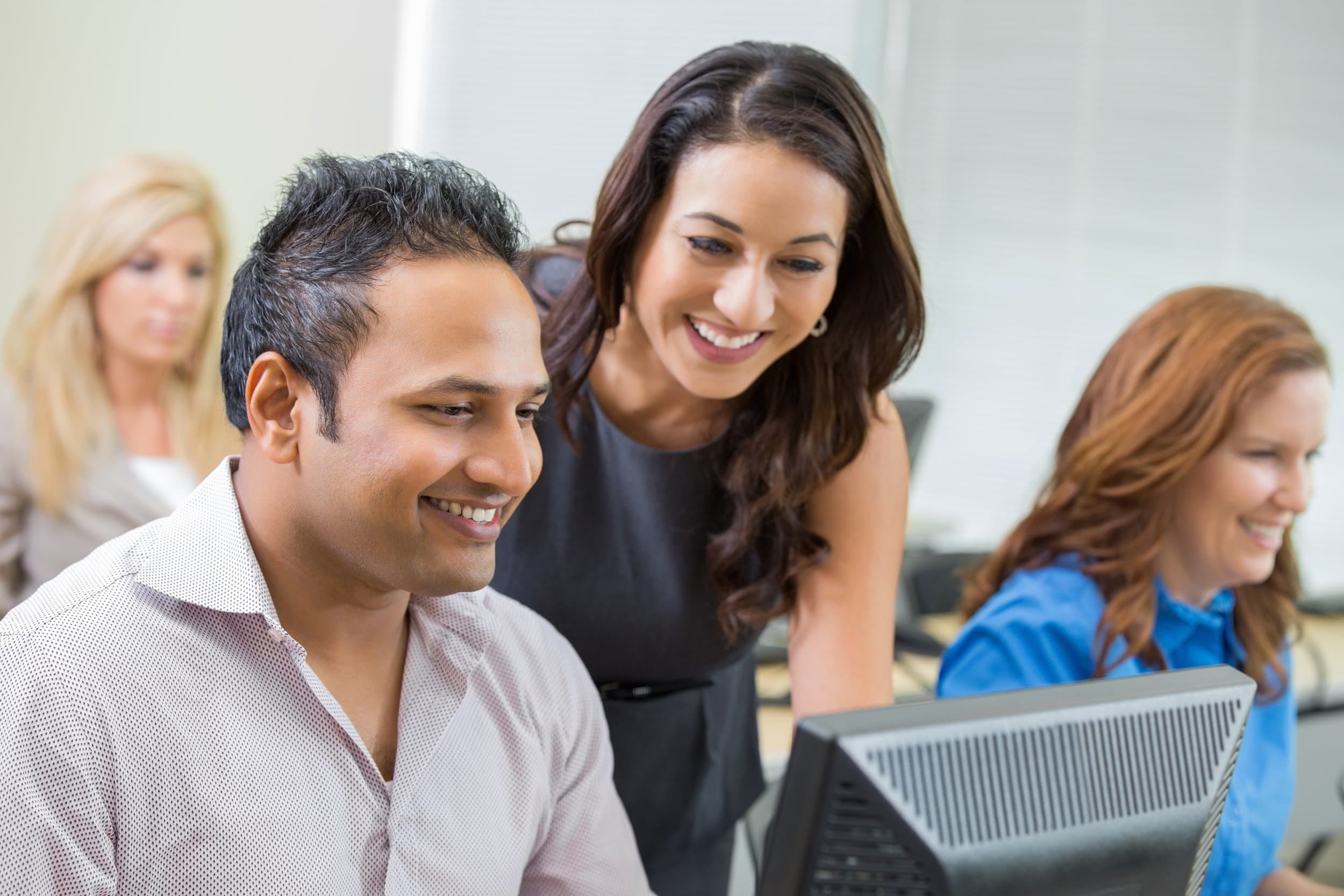 Two colleagues smiling while learning together at a computer